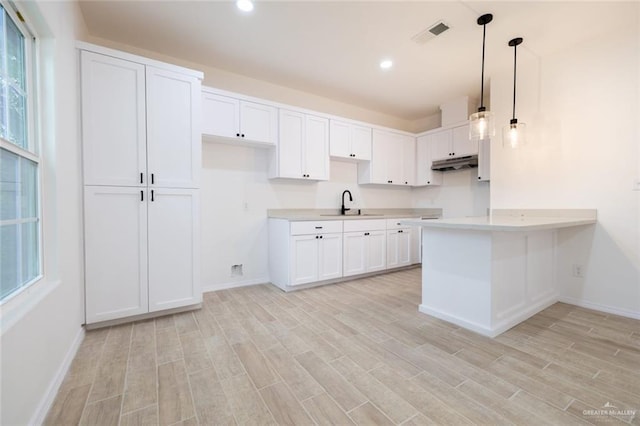 kitchen featuring visible vents, light wood-style flooring, a sink, under cabinet range hood, and a peninsula