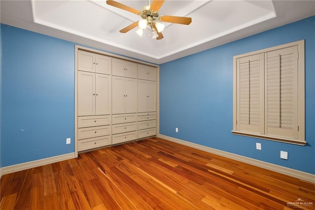 unfurnished bedroom with ceiling fan, a raised ceiling, and light hardwood / wood-style flooring