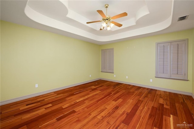 unfurnished room with a raised ceiling, wood-type flooring, and ceiling fan