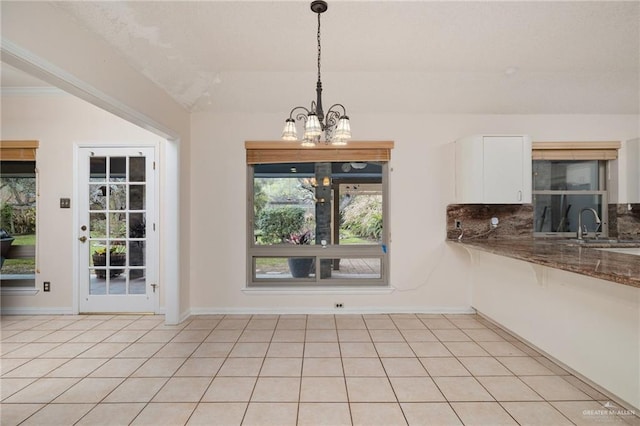 unfurnished dining area with light tile patterned floors, baseboards, a sink, and a notable chandelier