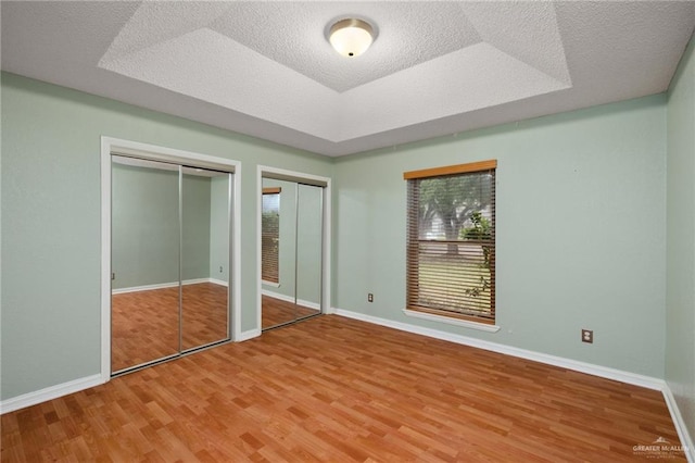 unfurnished bedroom with multiple closets, a tray ceiling, multiple windows, and wood finished floors