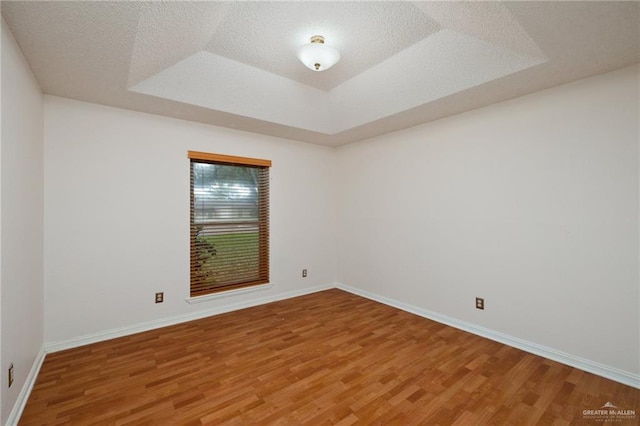 unfurnished room with a textured ceiling, a tray ceiling, wood finished floors, and baseboards