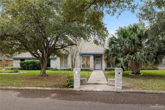 view of front facade featuring a front yard, stone siding, and roof with shingles