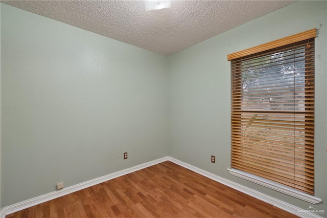 unfurnished room with a textured ceiling, wood finished floors, and baseboards