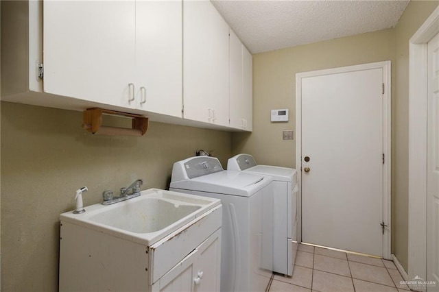 laundry area featuring light tile patterned floors, cabinet space, a sink, a textured ceiling, and independent washer and dryer