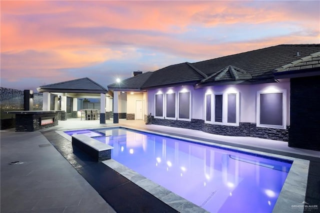 pool at dusk with a jacuzzi, a bar, and a patio