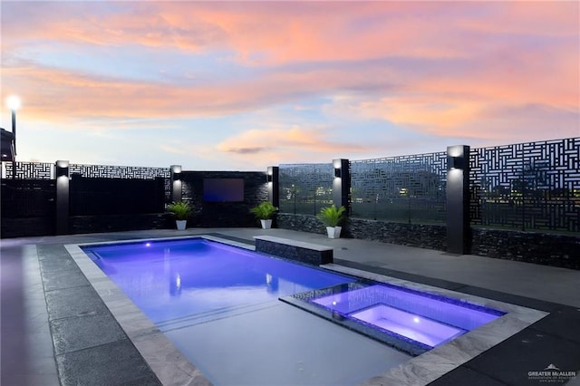 pool at dusk featuring an in ground hot tub