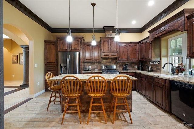 kitchen with decorative columns, light stone counters, stainless steel appliances, sink, and a center island