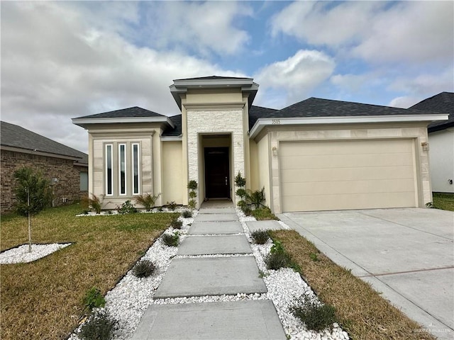 prairie-style home with an attached garage, a shingled roof, concrete driveway, stone siding, and a front lawn