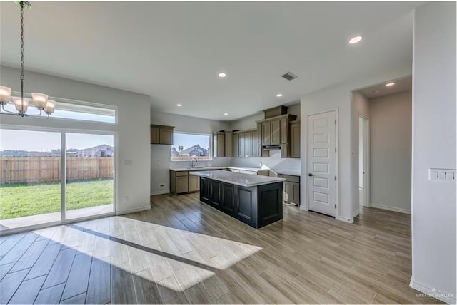 7409 55th St, Mcallen, TX 78573 - kitchen featuring a chandelier, light wood-style flooring, a center island, decorative backsplash, and under cabinet range hood