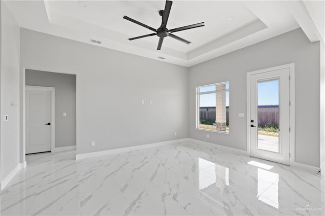 empty room with ceiling fan, visible vents, marble finish floor, and a raised ceiling