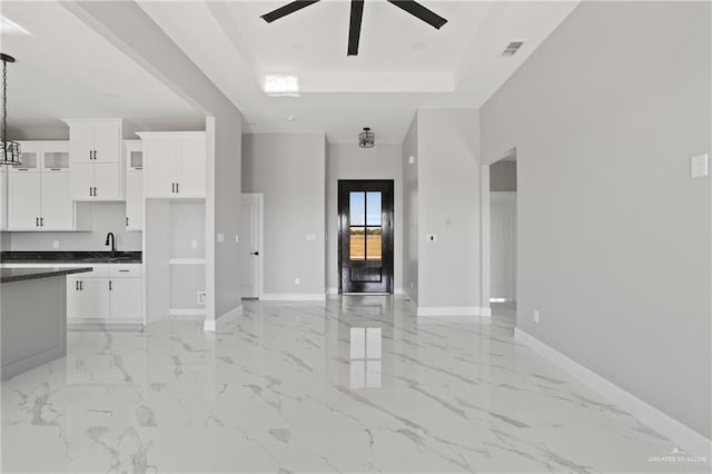 unfurnished living room with visible vents, baseboards, a sink, ceiling fan, and a tray ceiling
