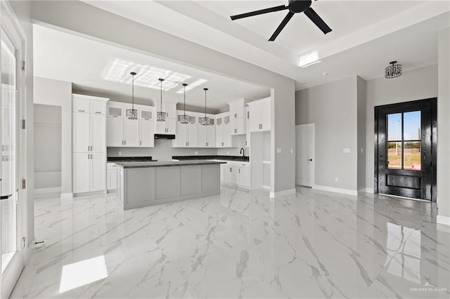 kitchen with ceiling fan, white cabinets, a kitchen island, dark countertops, and baseboards