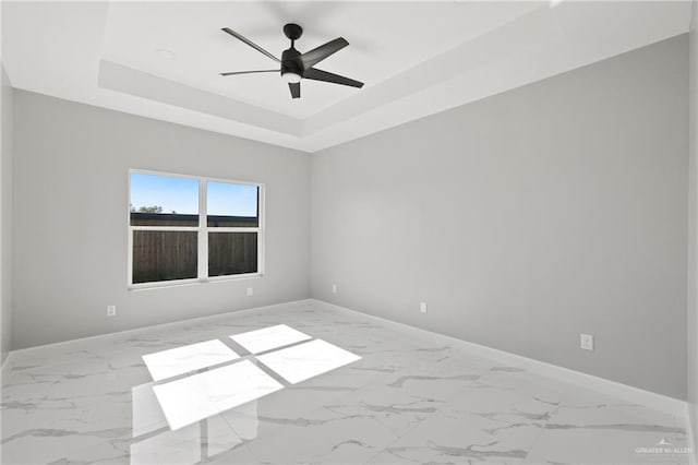 empty room featuring a tray ceiling, baseboards, a ceiling fan, and marble finish floor