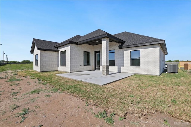rear view of property featuring cooling unit, a yard, roof with shingles, a patio area, and brick siding