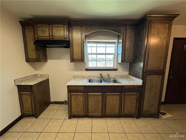 kitchen with dark brown cabinetry, light countertops, under cabinet range hood, and a sink