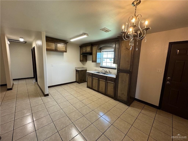 kitchen with visible vents, dark brown cabinetry, a chandelier, light tile patterned flooring, and a sink