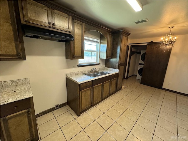 kitchen with visible vents, a sink, under cabinet range hood, a barn door, and stacked washer / dryer