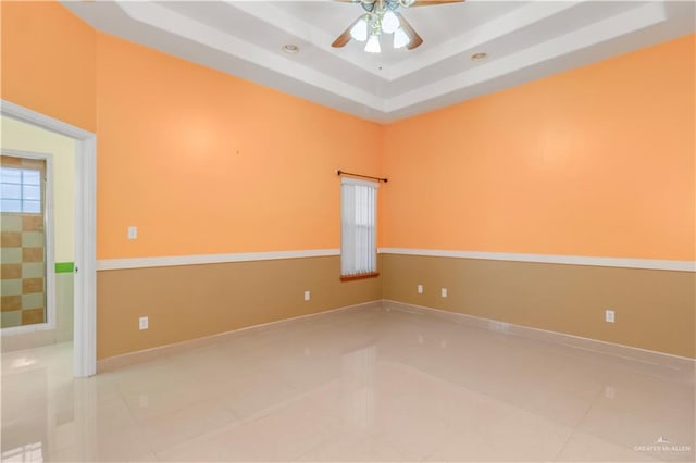 tiled empty room with ceiling fan and a tray ceiling