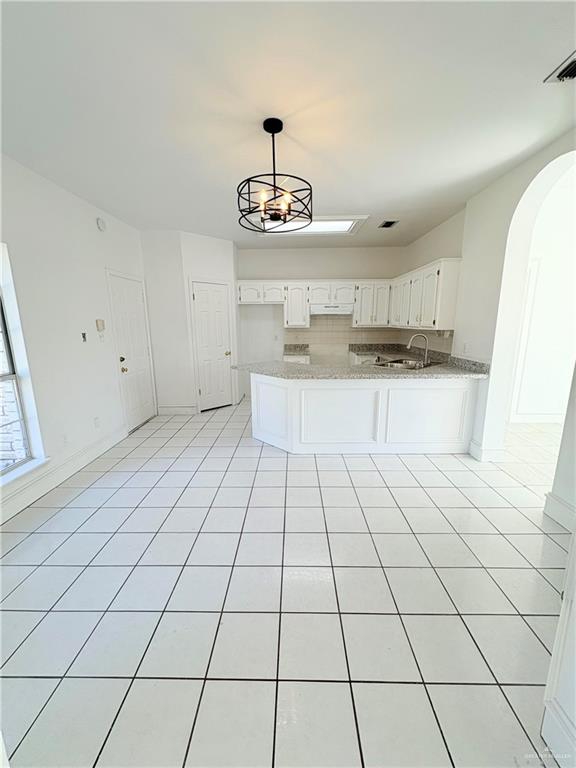 kitchen featuring kitchen peninsula, light stone countertops, light tile patterned floors, an inviting chandelier, and white cabinets