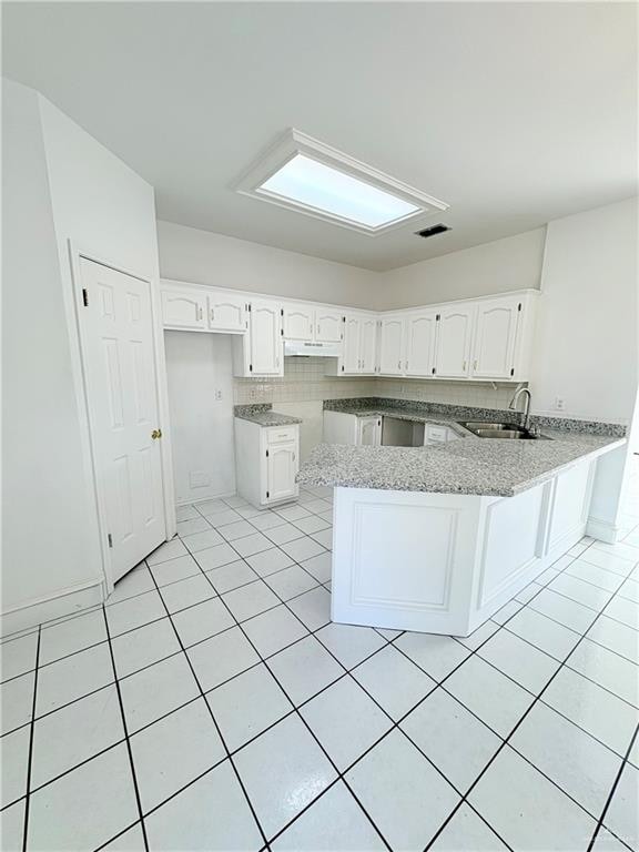 kitchen with white cabinets, sink, light tile patterned flooring, light stone counters, and kitchen peninsula