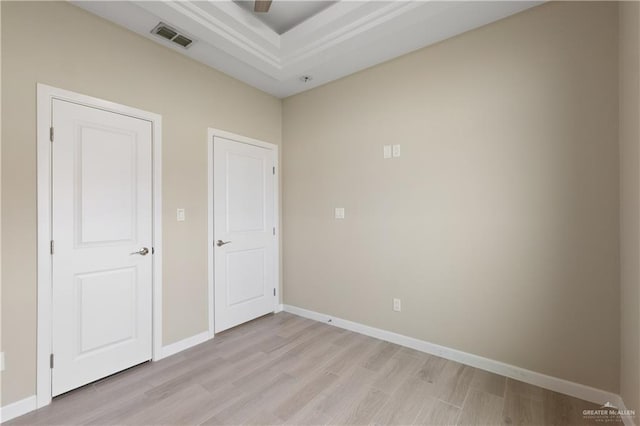 empty room featuring a tray ceiling, visible vents, baseboards, and light wood finished floors