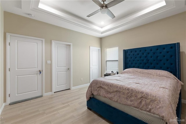 bedroom featuring a tray ceiling, recessed lighting, light wood-style floors, baseboards, and ceiling fan