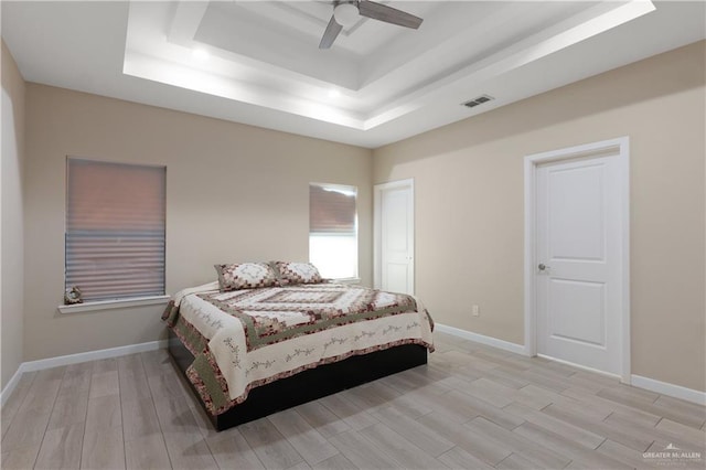 bedroom with visible vents, baseboards, light wood-type flooring, and a tray ceiling