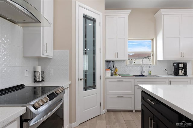 kitchen featuring electric range, a sink, light countertops, white cabinets, and exhaust hood