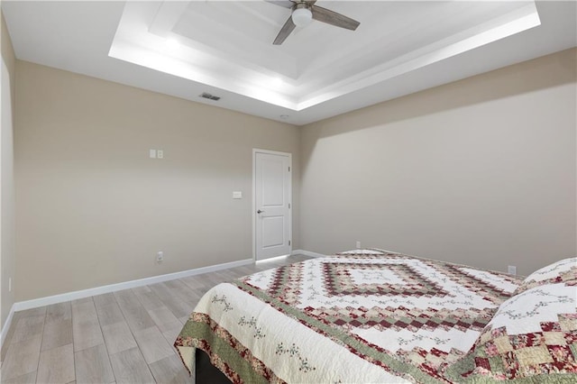 bedroom featuring a ceiling fan, baseboards, visible vents, a tray ceiling, and light wood-type flooring