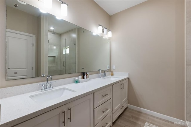 full bath with a shower stall, double vanity, baseboards, and a sink