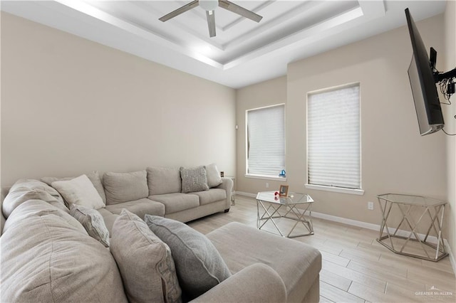 living room with light wood finished floors, ceiling fan, baseboards, and a tray ceiling