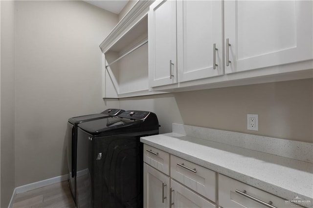 clothes washing area with cabinet space, washing machine and dryer, baseboards, and wood finished floors