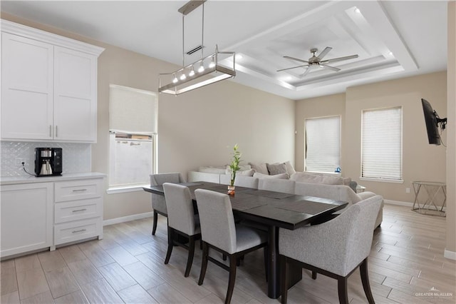 dining space featuring light wood finished floors, a healthy amount of sunlight, baseboards, and a tray ceiling