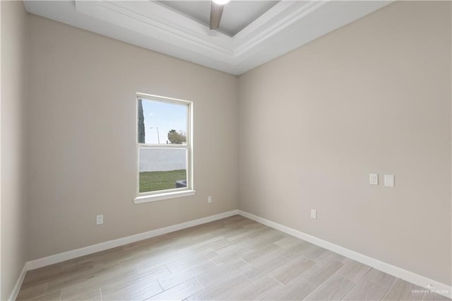 empty room featuring a raised ceiling, light wood-style flooring, and baseboards