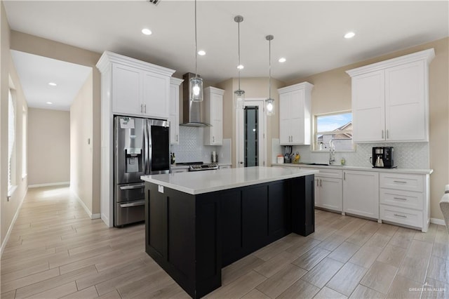 kitchen featuring a kitchen island, stainless steel appliances, light countertops, white cabinetry, and wall chimney range hood