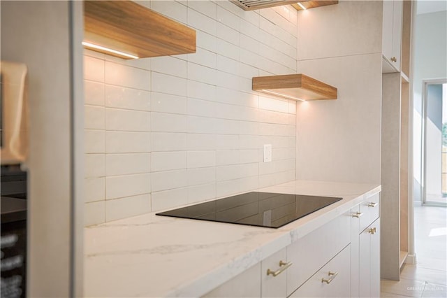 kitchen featuring light stone counters, black electric stovetop, and white cabinets