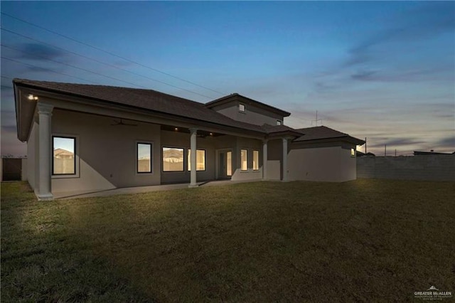 back house at dusk featuring ceiling fan, a patio area, and a yard