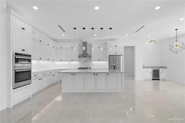 kitchen with pendant lighting, white cabinets, appliances with stainless steel finishes, wall chimney exhaust hood, and a kitchen island with sink