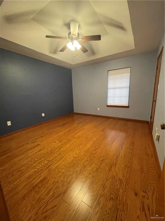 unfurnished room with ceiling fan, a tray ceiling, and light hardwood / wood-style floors