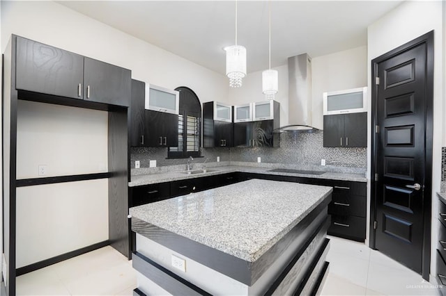 kitchen with hanging light fixtures, wall chimney exhaust hood, black electric cooktop, tasteful backsplash, and a kitchen island