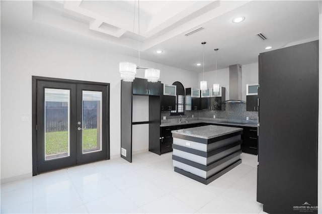 kitchen featuring french doors, a center island, wall chimney range hood, backsplash, and decorative light fixtures