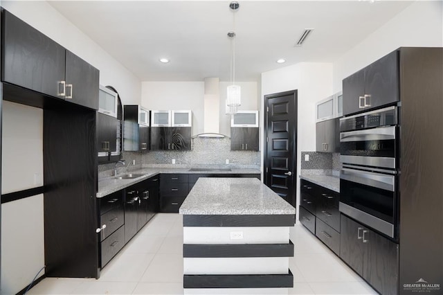 kitchen featuring a center island, wall chimney range hood, decorative backsplash, double oven, and decorative light fixtures