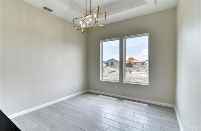 empty room with light hardwood / wood-style floors and an inviting chandelier