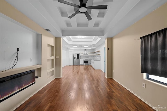 unfurnished living room with built in shelves, visible vents, a tray ceiling, wood-type flooring, and a glass covered fireplace