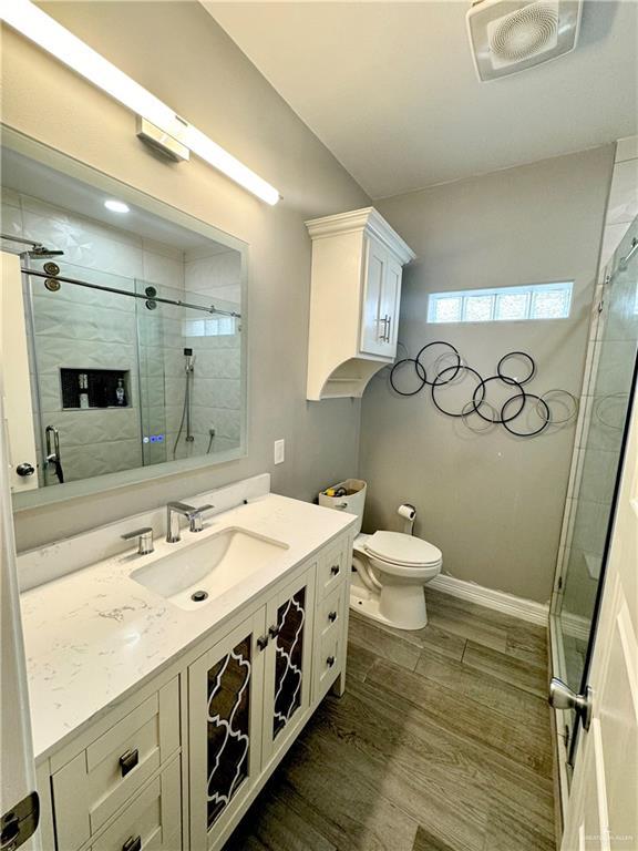 bathroom featuring a shower with door, vanity, and toilet