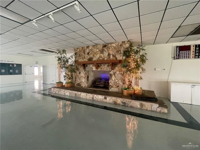 unfurnished living room with a paneled ceiling, concrete floors, and a stone fireplace