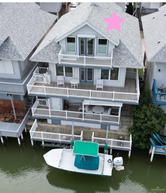 rear view of property with a water view, a balcony, and a shingled roof