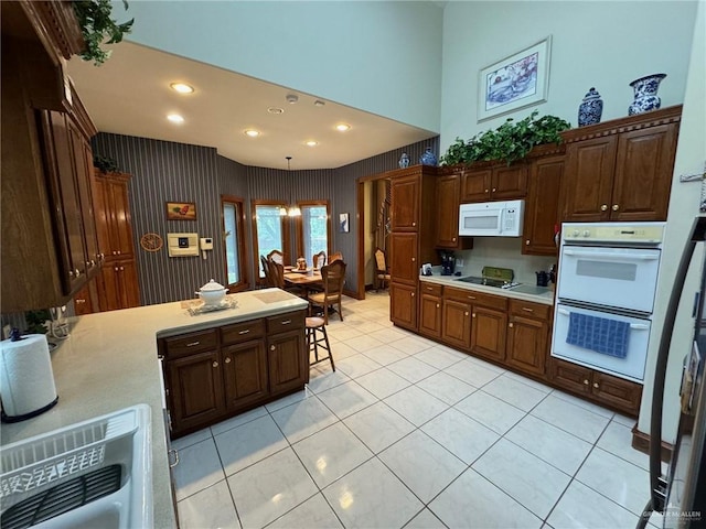 kitchen featuring light tile patterned flooring, a towering ceiling, pendant lighting, and white appliances