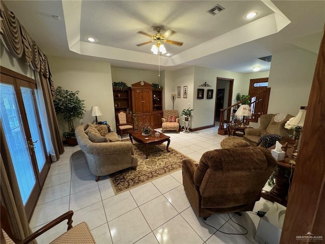 tiled living room with a tray ceiling and ceiling fan